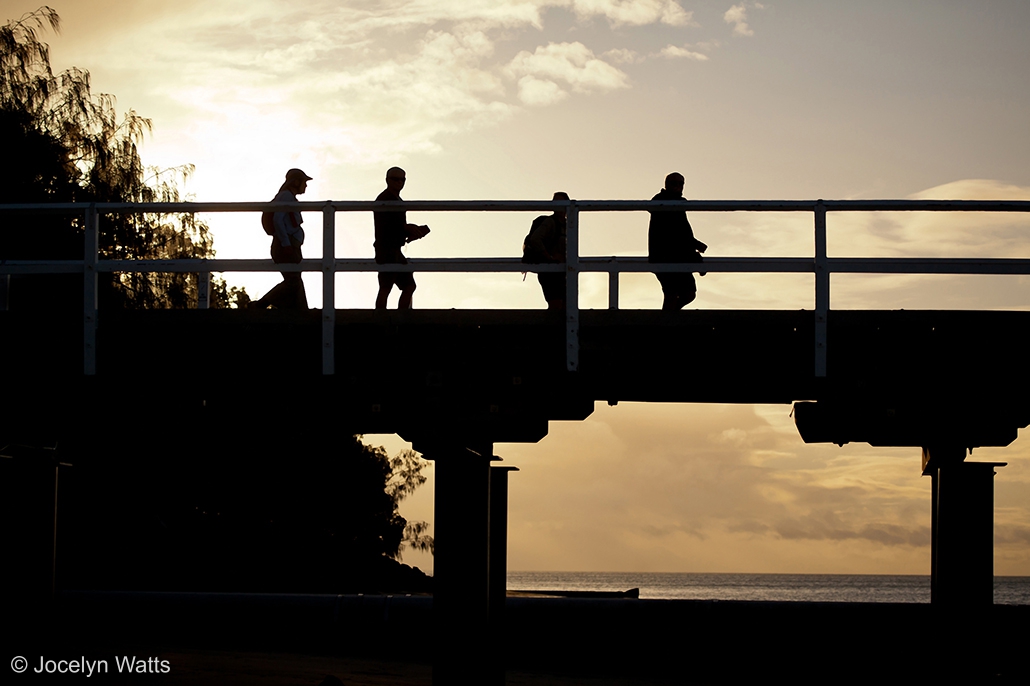 People walking along Urangan Pier at sunset in silhouette