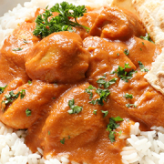 Butter chicken with rice, naan bread and cucumber raita served on a plate.