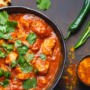 Butter chicken curry with naan bread and spices on a dark table