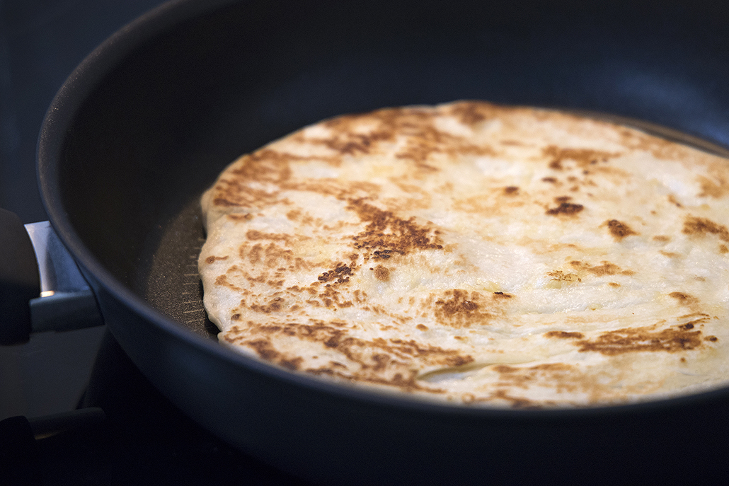 Store-bought naan heating in a Tefal non-stick frypan with golden charred spots.