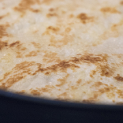 Store-bought naan heating in a Tefal non-stick frypan with golden charred spots.