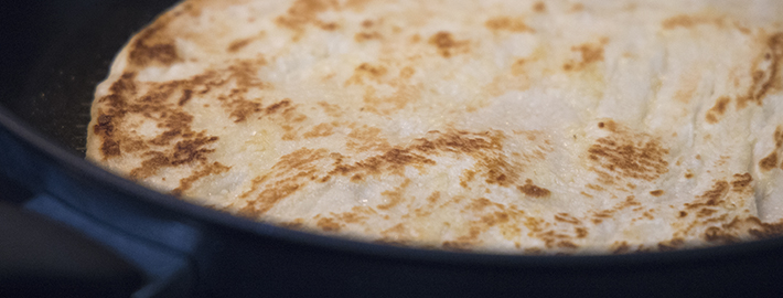 Store-bought naan heating in a Tefal non-stick frypan with golden charred spots.